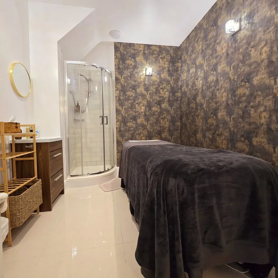 Artisa Spa treatment room with a dark-covered treatment bed and shower enclosure.