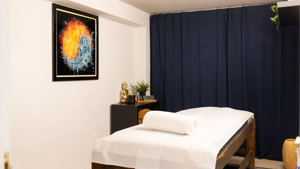 Meraki Spa treatment room with a treatment bed, dark curtains and framed artwork.