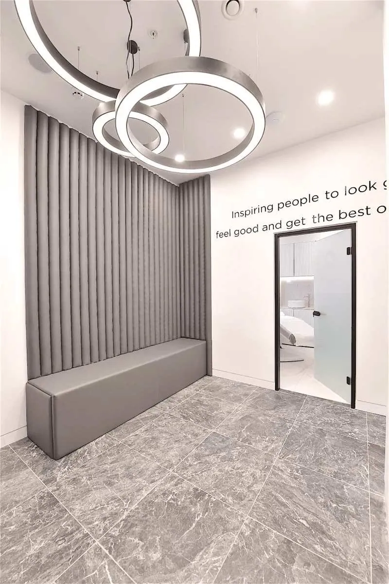 Waiting bench, circular pendant lights and a treatment-room doorway at Thérapie Clinic Uxbridge
