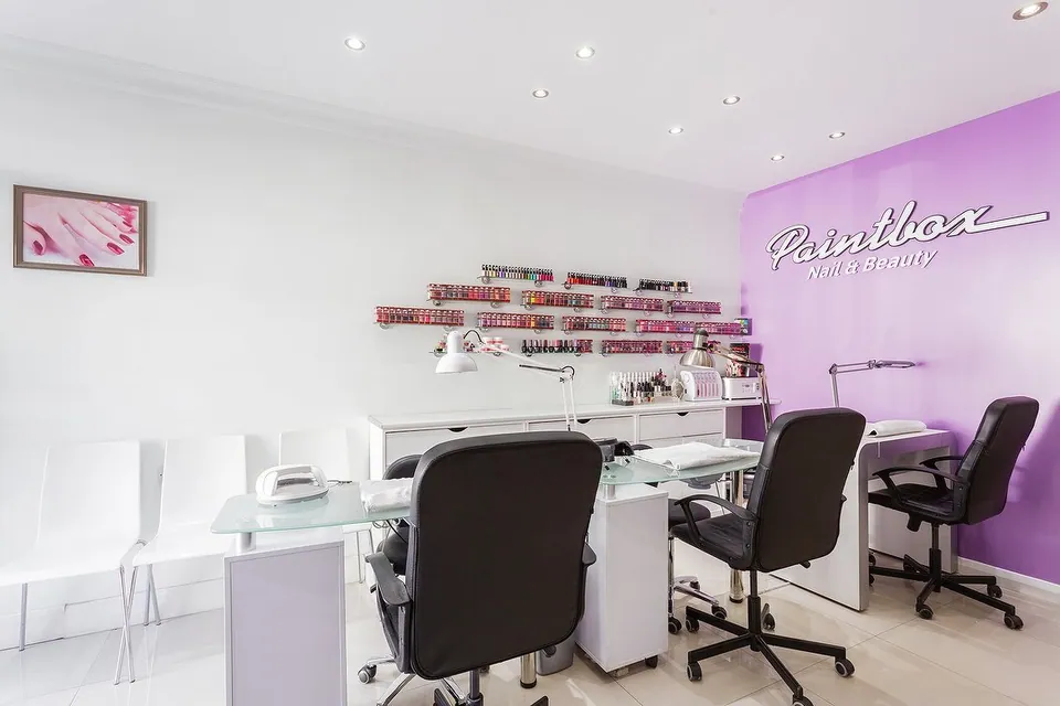 Paintbox manicure area with purple chairs and the salon name on a lilac wall.