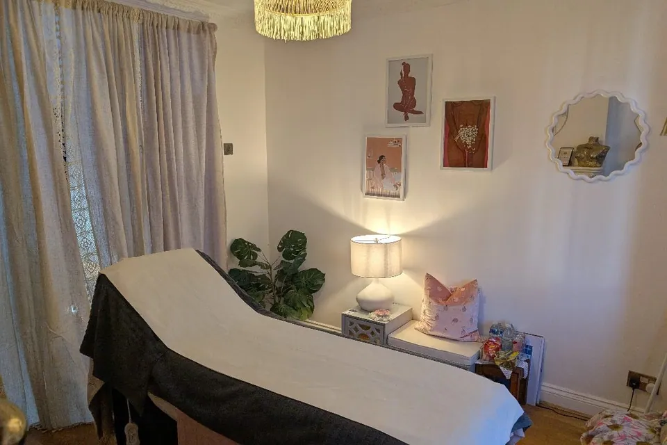 PeachBeauty treatment room with a covered couch, curtains and a lit bedside lamp.