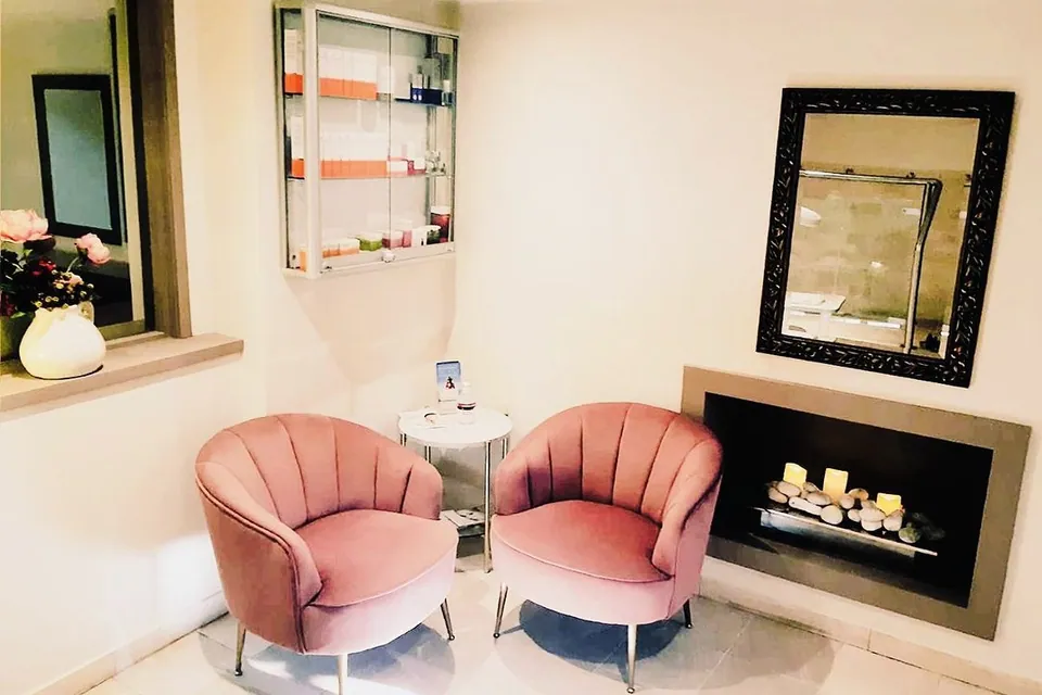 Shades seating area with two pink chairs, a fireplace and product display cabinet.